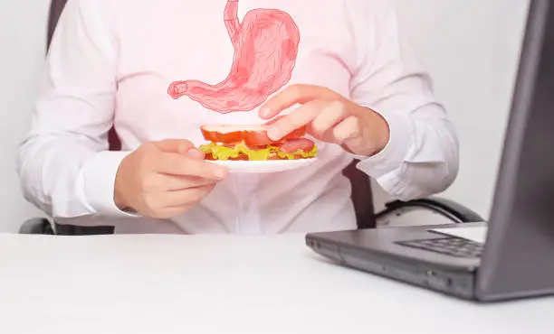 Photo of A male office worker holds a sandwich in his hands during lunch. The concept of unhealthy food, snacking, stomach pain. Gastritis and heartburn