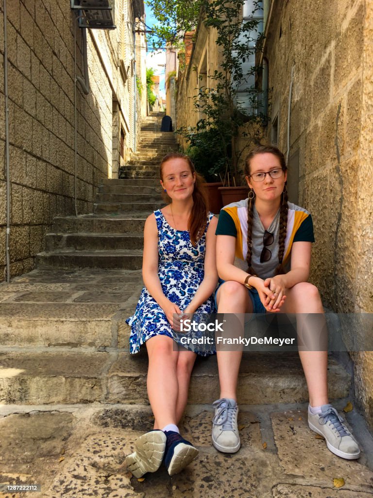 Friends chilling on a warm holiday afternoon, sitting on the chairs of the local village Two girls, aged 16 and 17, sitting together on the chairs of a small pass-way in the village of Cavtat, near the Adriatic beach. Staircase Stock Photo