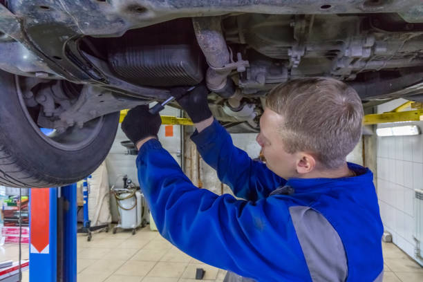 istock Mechanic working under a car at the garage. Technician wearing blue coverall and using a wrench. Car is on a hydraulic lift 1287223348