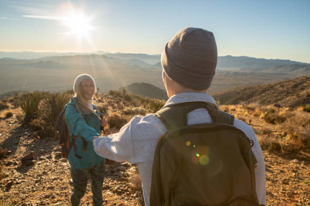 istock Hikers reach mountain top at sunrise, woman pulls man with hand 1287228439