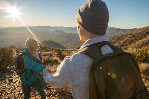 istock Hikers reach mountain top at sunrise, woman pulls man with hand 1287228578