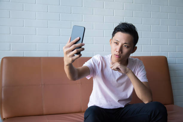 istock Asian man taking selfie with smart phone while relaxing on sofa 1287230100