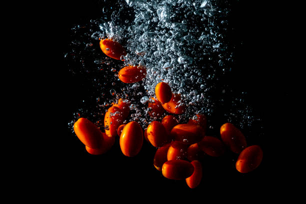 Lots of cherry tomatoes falling into the water. Black background.