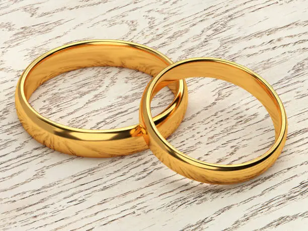 Two wedding gold rings lie next to each other on wood background. 3d rendering