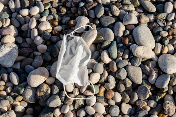 brudna używana jednorazowa medyczna maska na kamienistej plaży drogą morską. odpady podczas covid-19. zanieczyszczenie spowodowane pandemią coronavirus - 5428 zdjęcia i obrazy z banku zdjęć