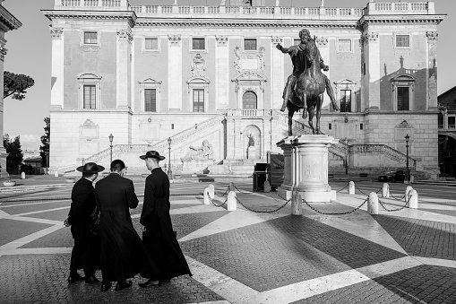 Rome, Italy, July 15 -- Some Catholic priests visit in solitude the Capitoline Hill square (Piazza del Campidoglio), taking photos and selfies. At right the bronze copy of the majestic equestrian statue of Emperor Marcus Aurelius. The original statue of Marcus Aurelius is kept inside the Capitoline Museums. The square was designed by Michelangelo Buonarroti and currently the Campidoglio is the seat of the Municipality of Rome. Image in High Definition format