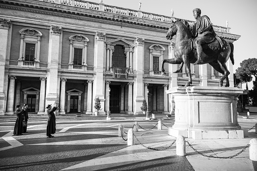 Rome, Italy, July 15 -- Some Catholic priests take photos in solitude in the Capitoline Hill square (Piazza del Campidoglio). At right the bronze copy of the majestic equestrian statue of Emperor Marcus Aurelius. The original statue of Marcus Aurelius is kept inside the Capitoline Museums. The square was designed by Michelangelo Buonarroti and currently the Campidoglio is the seat of the Municipality of Rome. Image in High Definition format