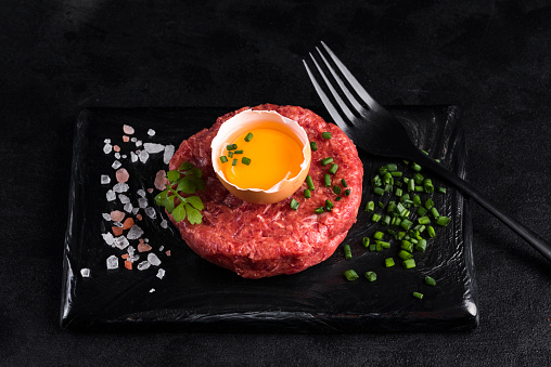 Tartare on a black ceramic board with green onions, egg yolk and salt.