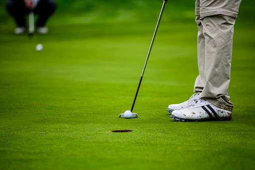 Close-up of a golf player who with a putt pocket the ball on the green