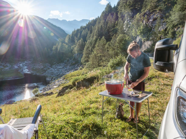 istock Man cooks on portable barbecue outside his van, mountain view 1287252182