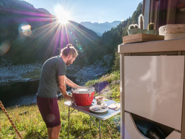 istock Man cooks on portable barbecue outside his van, mountain view 1287252295