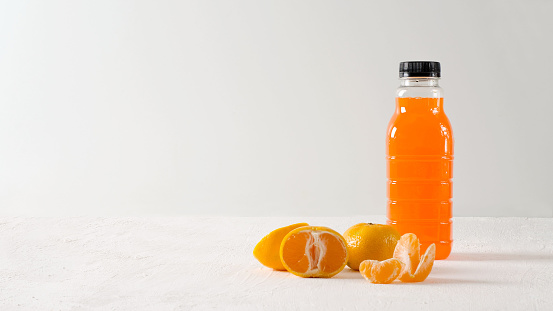 Tangerine drink in bottle on light background with tangerines, copy space and selective focus