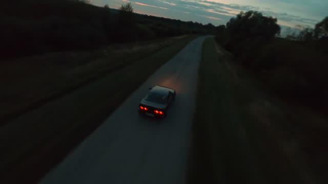 Sport black jdm vehicle drives along empty narrow rural road and does police turn drifting at forest in dark evening first point view cinematic aerial shot by fpv racing drone