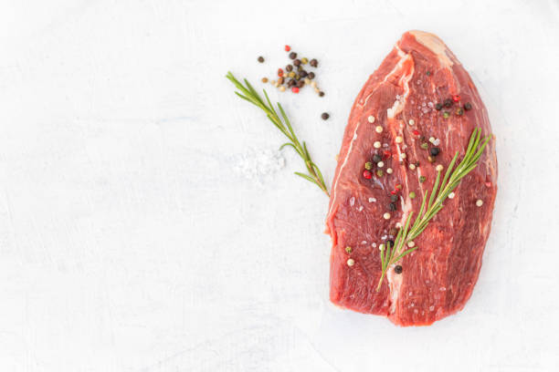 istock raw beef meat with spices on a white stone background. 1287254140