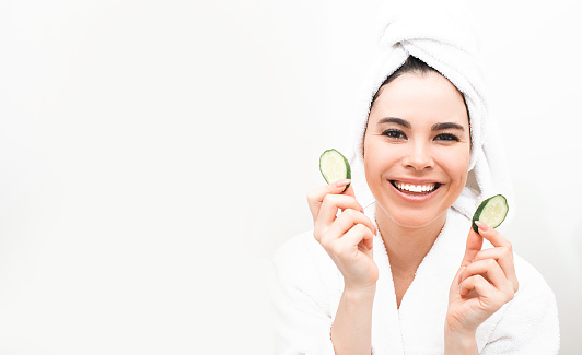 Cucumber mask for smooth skin face. Mixed race woman, with towel around head holding slices cucumber for skin rejuvenation