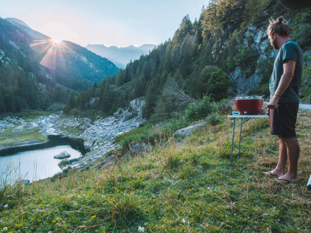 istock Man cooks on portable barbecue outside his van, mountain view 1287255964