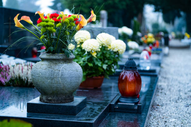 Fog going up in the morning, quiet path on a graveyard, grave with beautiful flowers and a candle.
