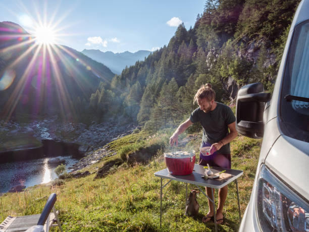 istock Man cooks on portable barbecue outside his van, mountain view 1287257563