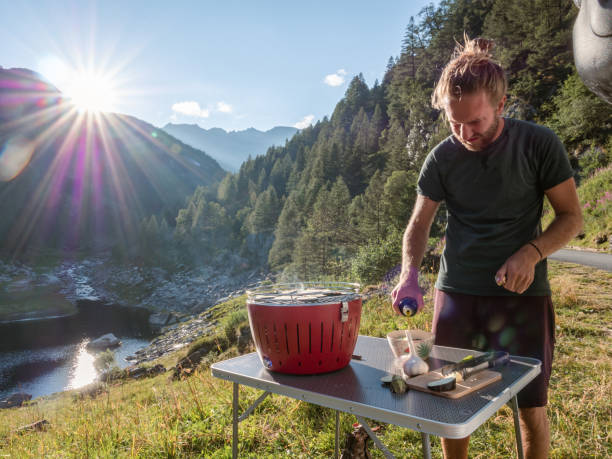 istock Man cooks on portable barbecue outside his van, mountain view 1287257878