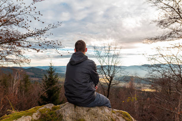 istock Young man sitting on mountain in autumn forest from back. Czech landscape 1287259069