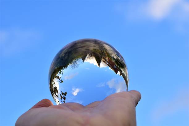 istock Blue sky and some trees trough a crystal lens ball on a human hand 1287261988