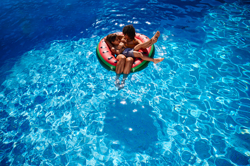African-american mother and son floating in watermelon swim ring in a infinite pool
