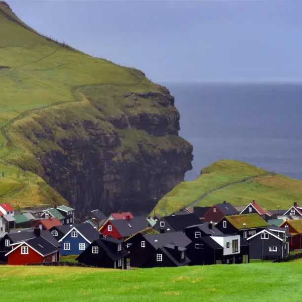 Small village in front of the natural harbor in a rock canyon in Gjogv on a sunny afternoon on Faeroe Islands.