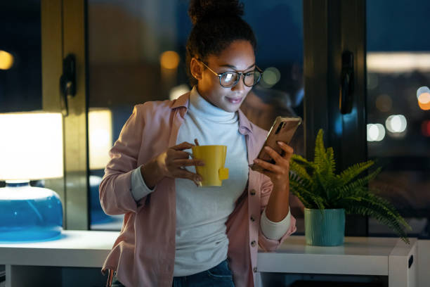 istock Pretty young entrepreneur woman using her smart phone while drinking a cup of coffee standing in the office. 1287263551