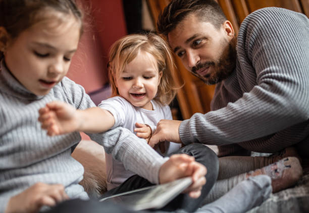 istock Single young father with his daughters reading a book on a digital tablet at home 1287263808