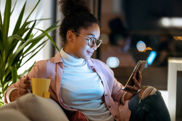 istock Happiness young entrepreneur woman using her smart phone while drinking a cup of coffee sitting on couch in the office. 1287263886