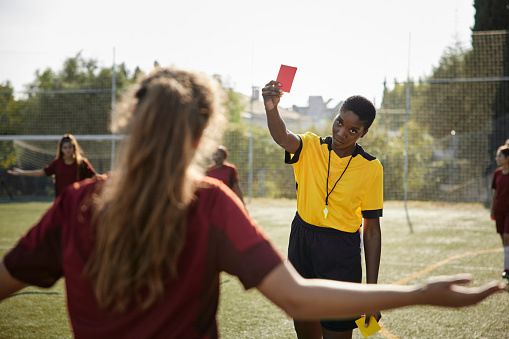 Soccer female african-american referee shows red card for penalty to female soccer player and her team upset in red sports uniform