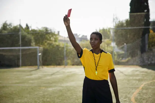 Portrait of african-american female referee holding red card in yellow uniform
