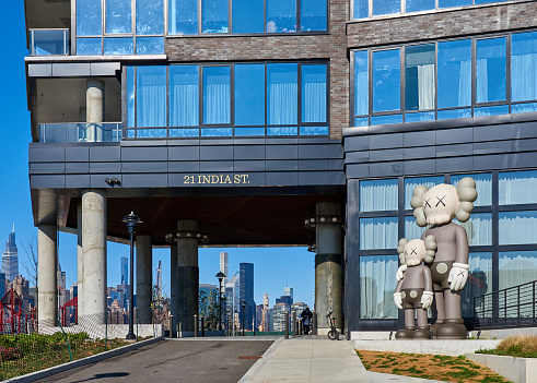 Brooklyn, NY - November 14 2020: The porte-cochere entrance to 21 India Street, residential skyscraper in Greenpoint is flanked by a large-scale sculpture of two figures by the artist KAWS. The building is located on the East River waterfront, designed by Ismael Leyva Architects. The skyline of Manhattan is seen the background.