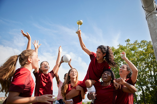 Group of happy multi-ethnic female soccer players celebrating game victory with trophy