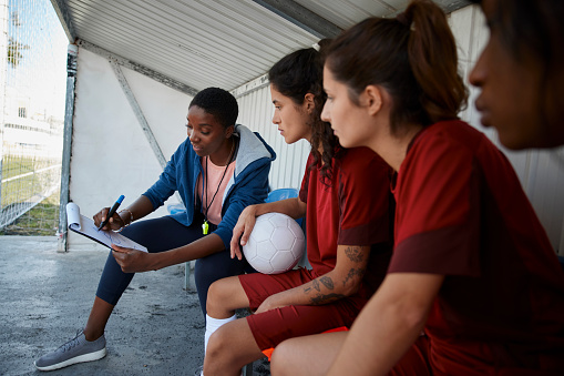 African-american soccer coach explaining match strategies to her female soccer team before practice
