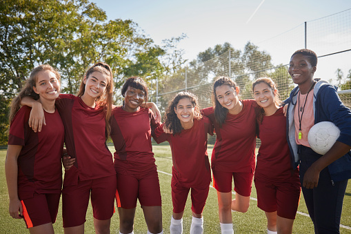 Female coach and soccer team smiling looking at camera holding ball