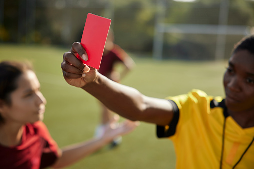 Close-up of african-american female referee holding red card to soccer player during match
