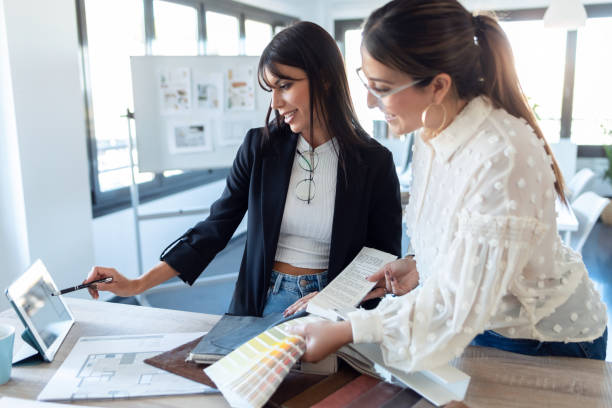 zwei schöne junge designerinnen, die in einem designprojekt arbeiten, während sie materialien im büro auswählen. - innenarchitekt stock-fotos und bilder