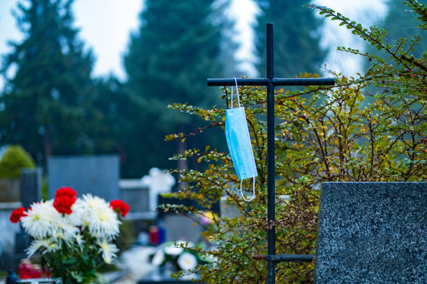 istock Death by virus. Face mask on a iron cross in the cemetery. 1287266437