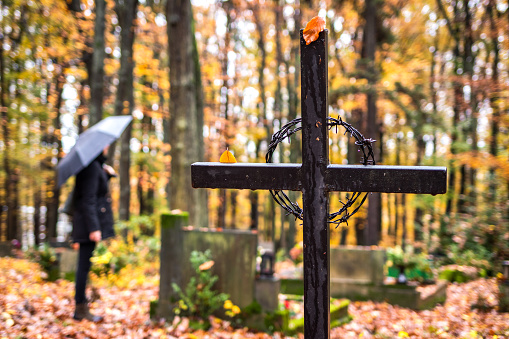Religious cross in cemetery. Mourning woman in black standing next to tombstoneat graveyard  in rain. Silent memory for dead relatives