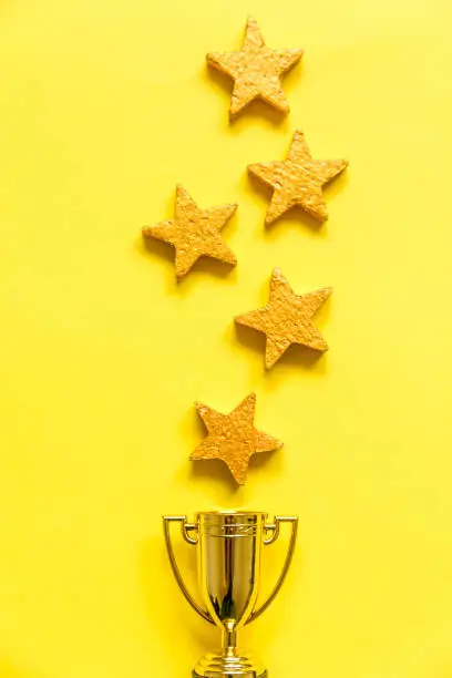 Photo of Simply flat lay design winner or champion gold trophy cup and 5 stars rating isolated on yellow background. Victory first place of competition. Winning or success concept. Top view copy space