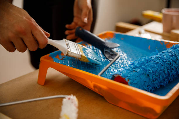 istock Dipping paintbrush and paint roller in a tray with blue paint 1287270176