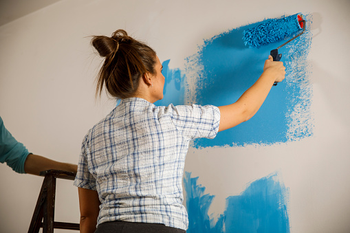 Low angle view of diligent young woman and her boyfriend renovating their apartment and painting the walls with paint roller in blue.