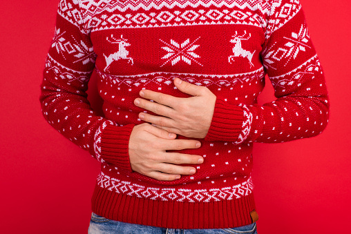 Bellyache concept. Close up photo of men in red winter sweater with deers holding his stomach isolated on red background