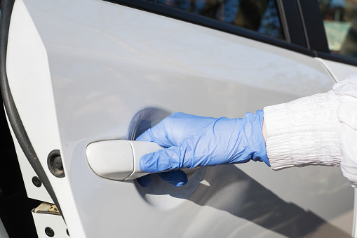 woman's hand in blue medical glove opens white car door. New reality, protective and preventive measures against covid pandemic. Health care concept