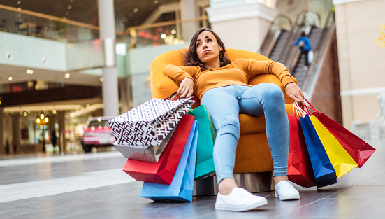 Mujer joven cansada y estresada está acostada y descansando en la silla con muchas bolsas de compras en el centro comercial photo