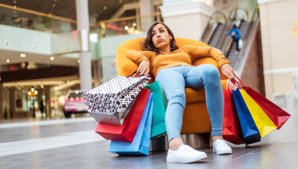 giovane donna stanca e stressata giace e riposa sulla sedia con molte borse della spesa nel centro commerciale - christmas shopping foto e immagini stock