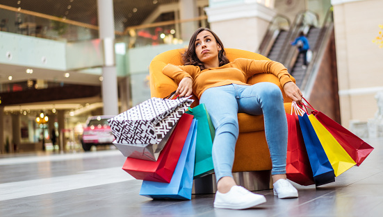 Tired and stressed young woman is lying and resting in the chair  with many shopping bags in the mall