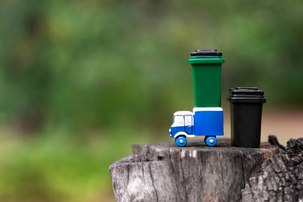 istock Toy garbage truck and garbage cans standing on a tree hemp against a blurred forest background. Selective focus, copy space. 1287288512