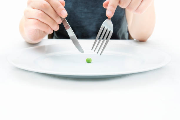istock Woman eating a small green pea using knife and fork. 1287288546